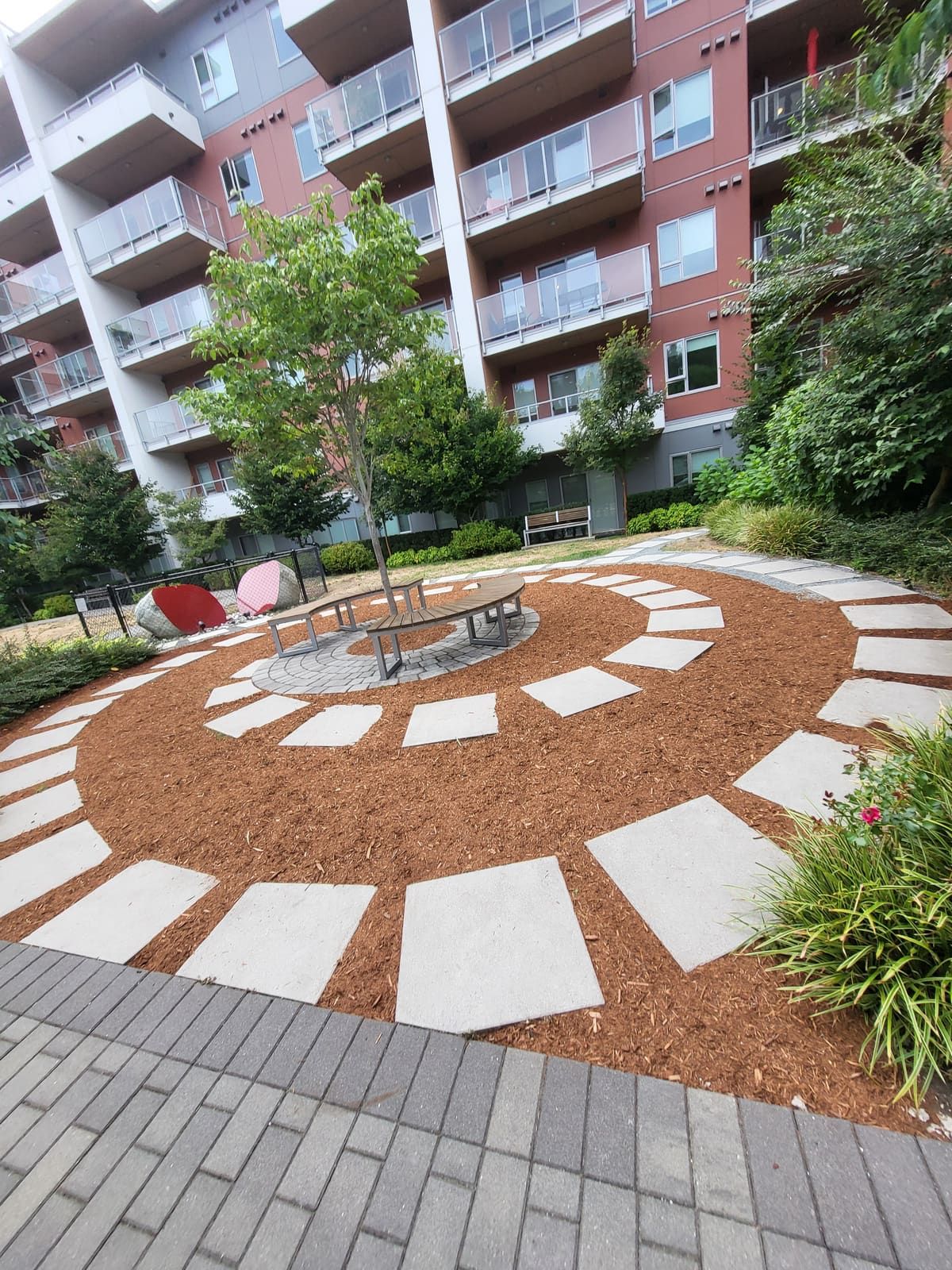 Spiral walkway of concrete pavers set in fresh cedar mulch around a circular tree bench in a strata courtyard